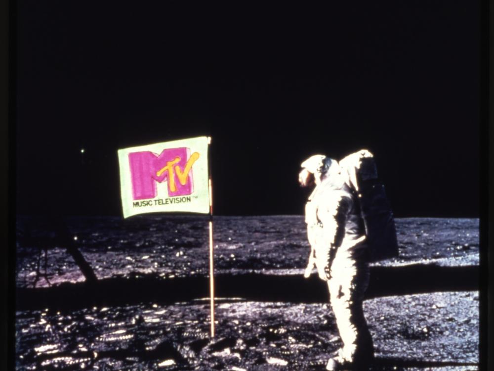 A photo of an astronaut on the Moon standing next to a flag with the MTV logo on it.