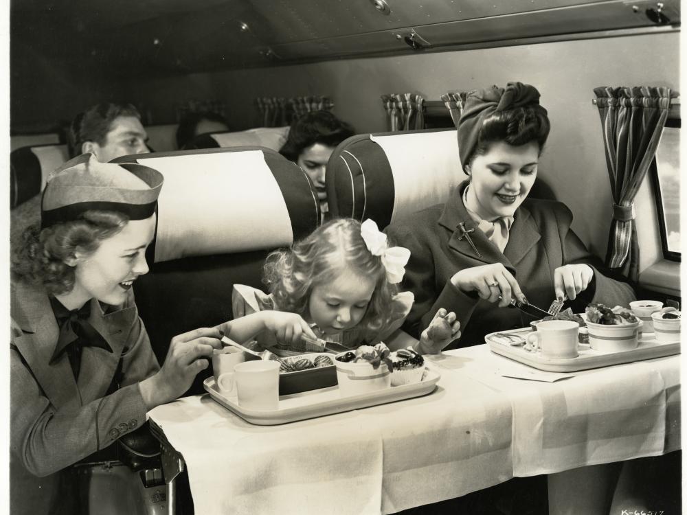 United Airlines flight attendant assisting passengers wearing the United Airlines flight attendant cap (1946)