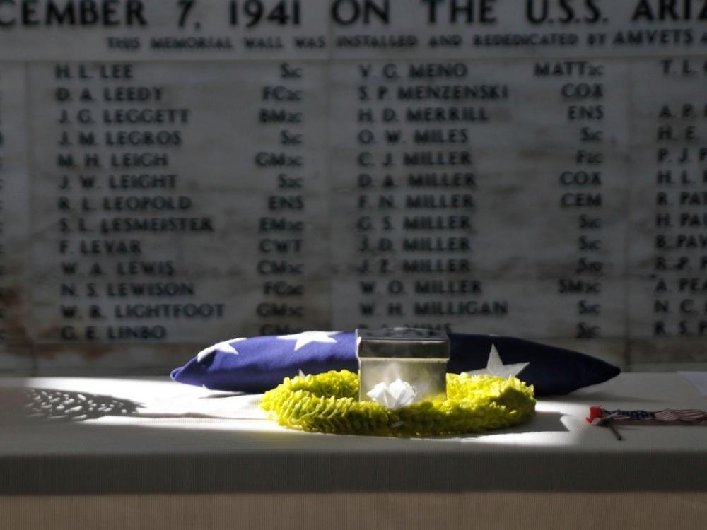 The remains of retired Master Chief Glenn Harvey Lane sit on a table at the USS Arizona Memorial with names written on a wall in the background.