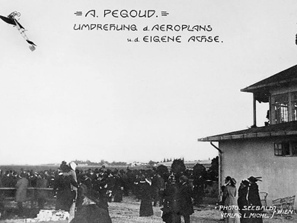 A crowd watching an airplane do a loop in the air. Text on the photo says "A. Pegoud, Umdrehung d. Aeroplans, u.d. Eigene Achse"