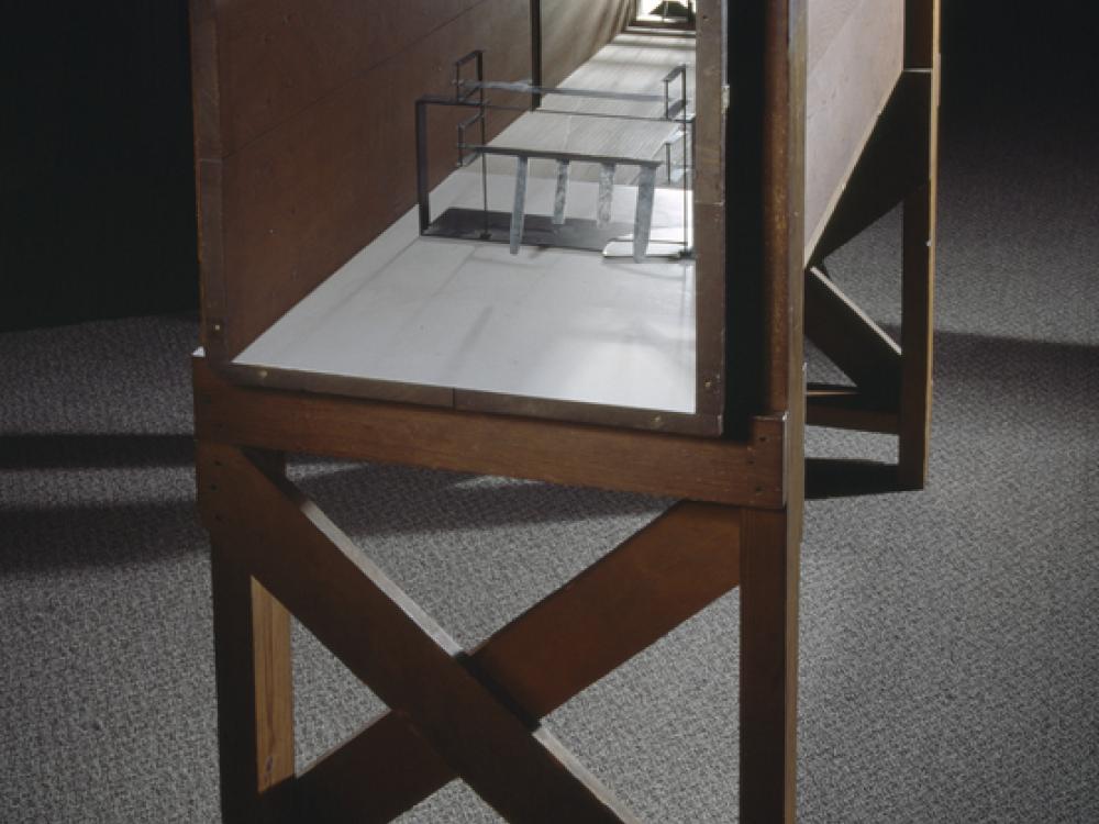 Wooden frame supporting hollow rectangular box-shaped wind tunnel.