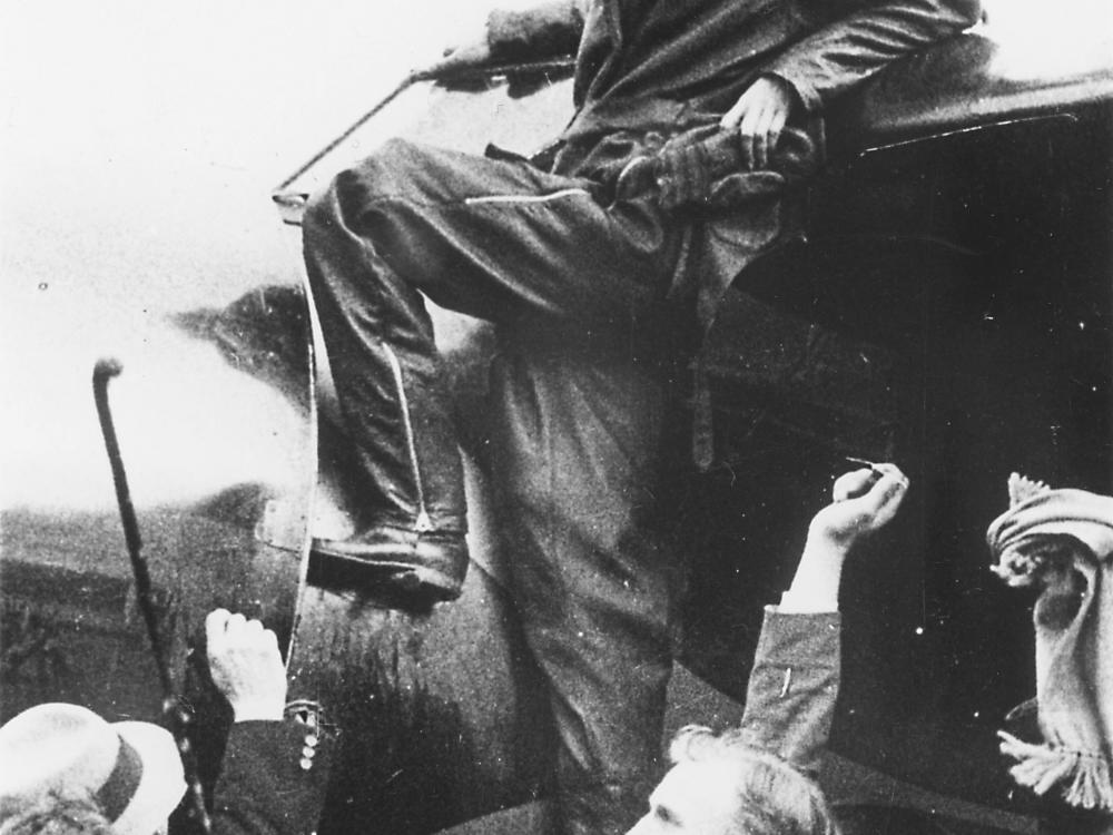 A woman stand by the wing of an aircraft, smiling, while others surround her.