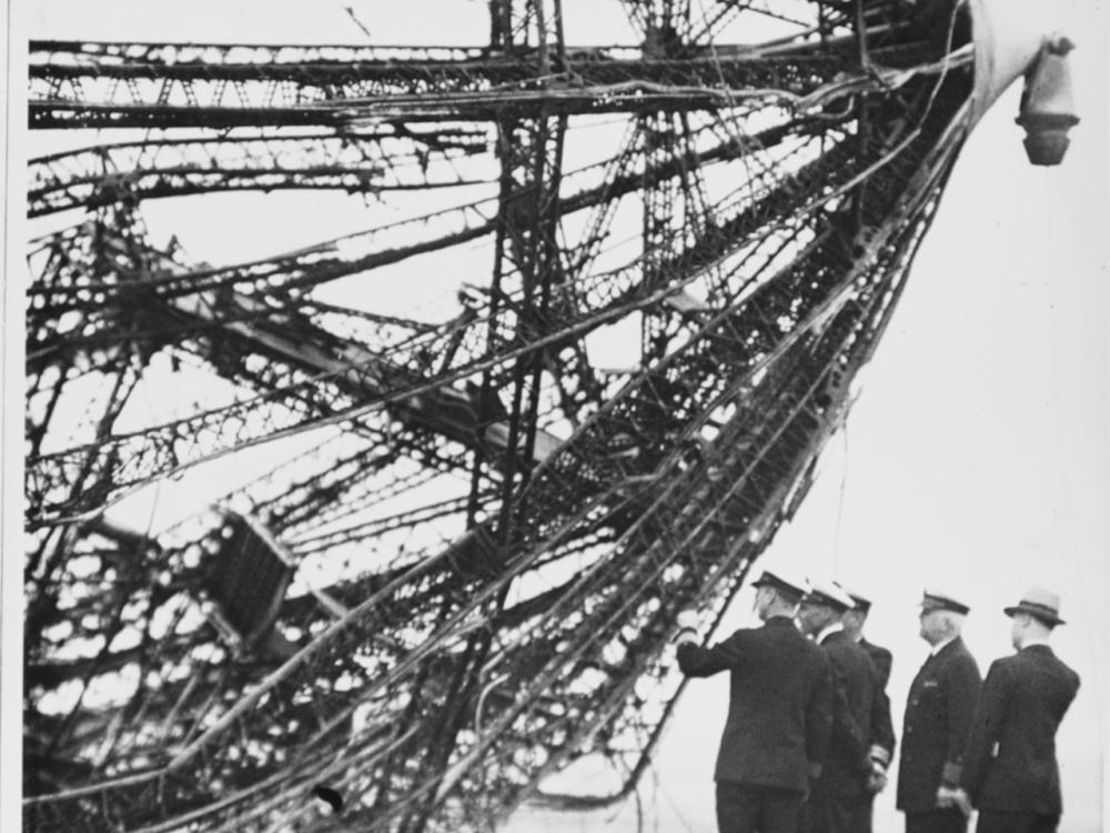 Black and white image of uniformed individuals looking at wreckage from a crash.