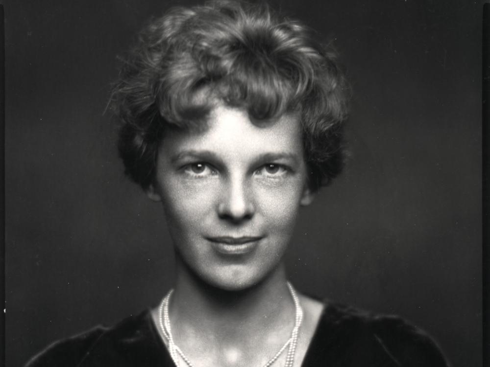 A half body portrait shot of a woman with short hair. One of her necklace has a pendant that looks like wings.