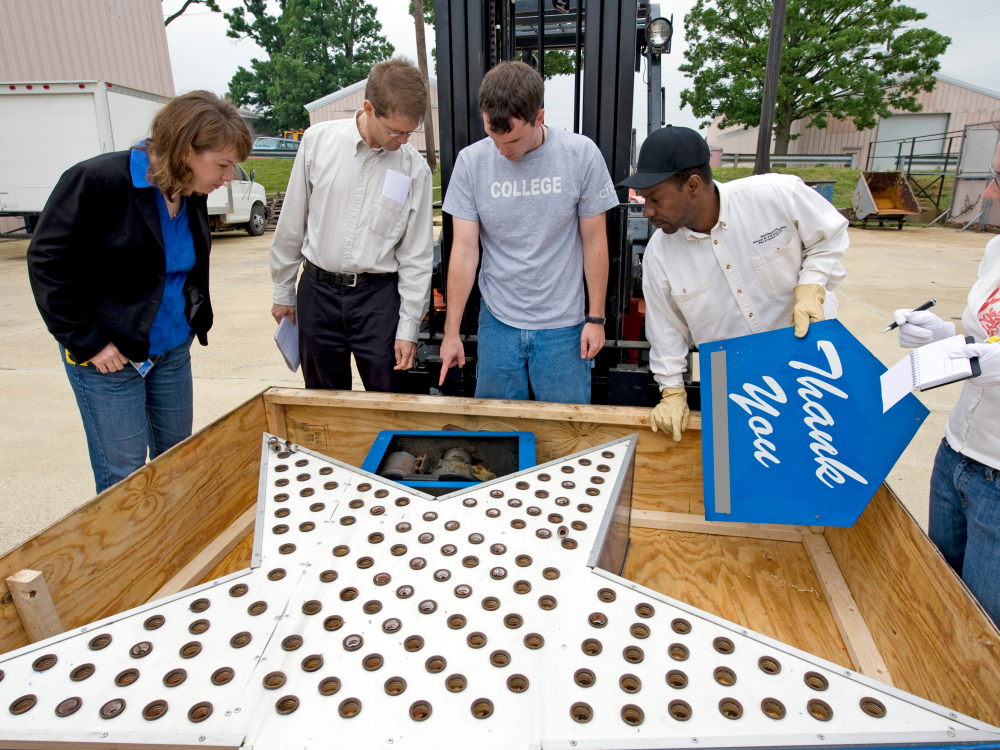 Five people stand around a crate containing a large silver star covered in lights.