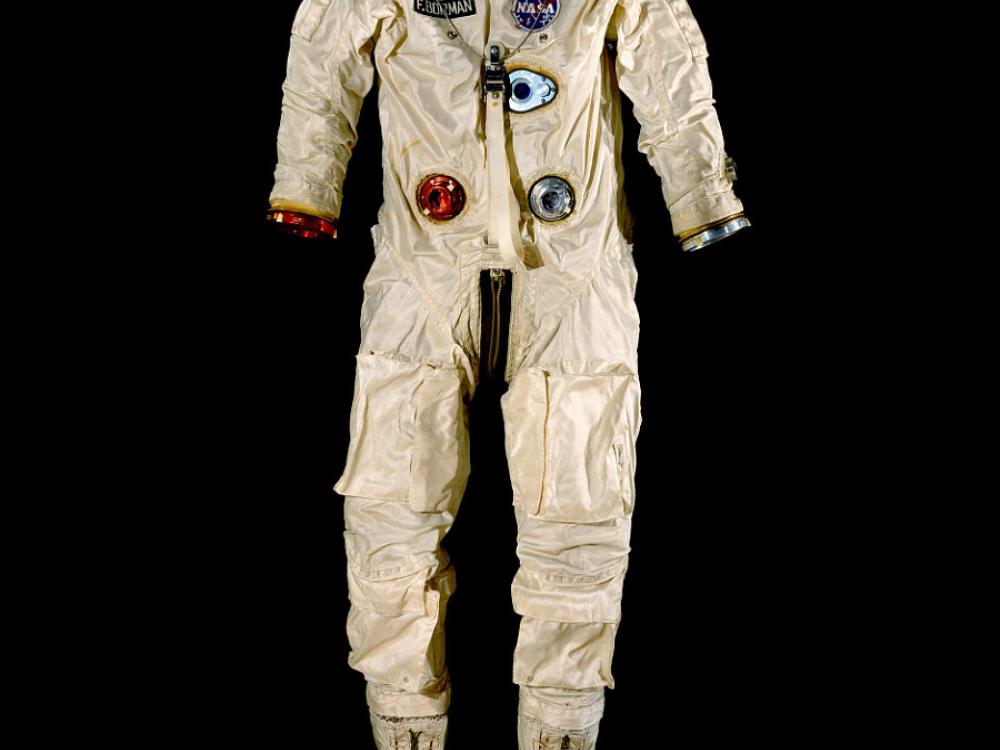 A cream colored space suit with accents of red and blue posed against a black background. There are boots attached but no helmet or gloves.