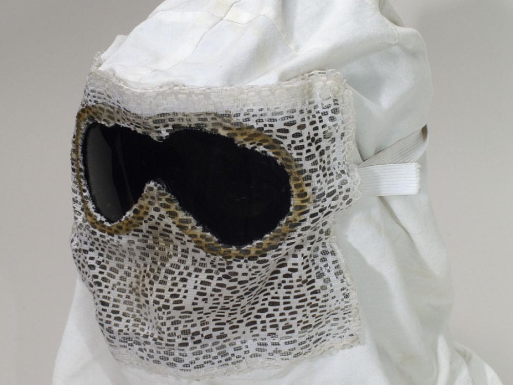 A white hood with goggles propped up for a photograph. The front of the hood has mesh on it, presumably to breathe.