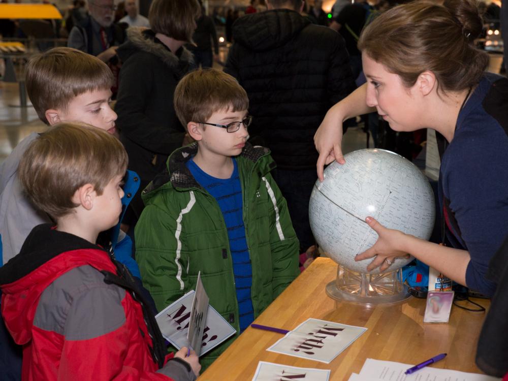An educator shows three young boys a model of the moon. 