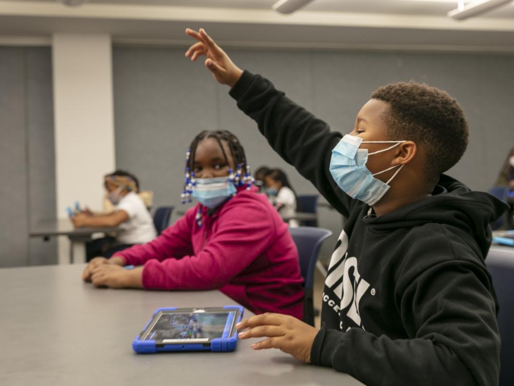 A young man wearing two surgical masks raises his hand with enthusiasm. 