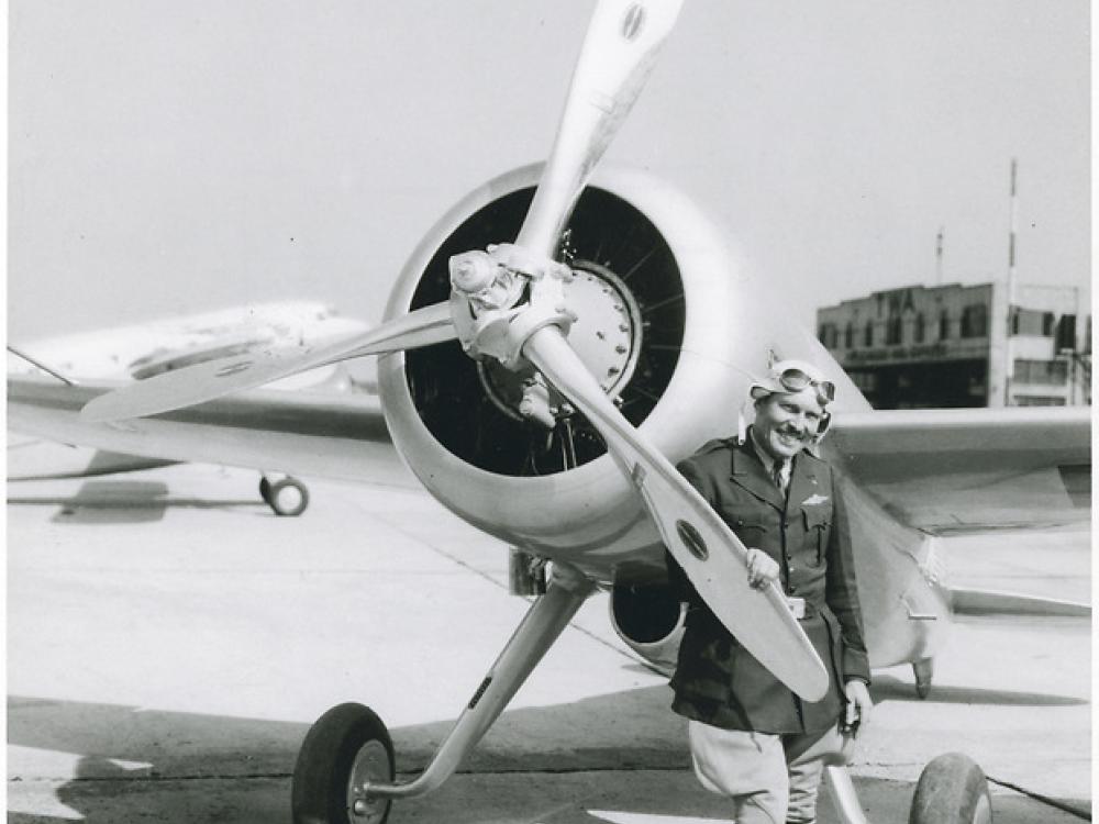 View of the Turner-Laird LTR-14 "Pesco Special" on the ground; pilot Roscoe Turner, in uniform, poses standing behind one blade of propeller at left side of nose of the aircraft.