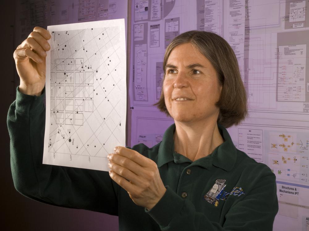 A woman examines a piece of paper as she holds it up. The paper has different boxes and dots on it.