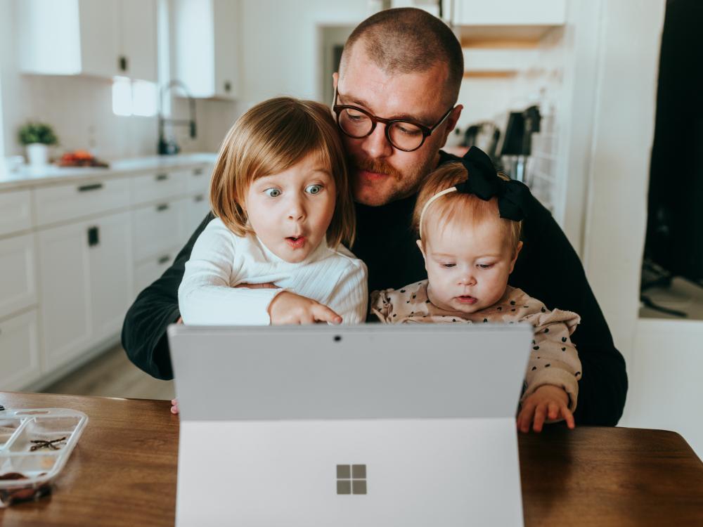 A man holds two young children who look at a surface screen.