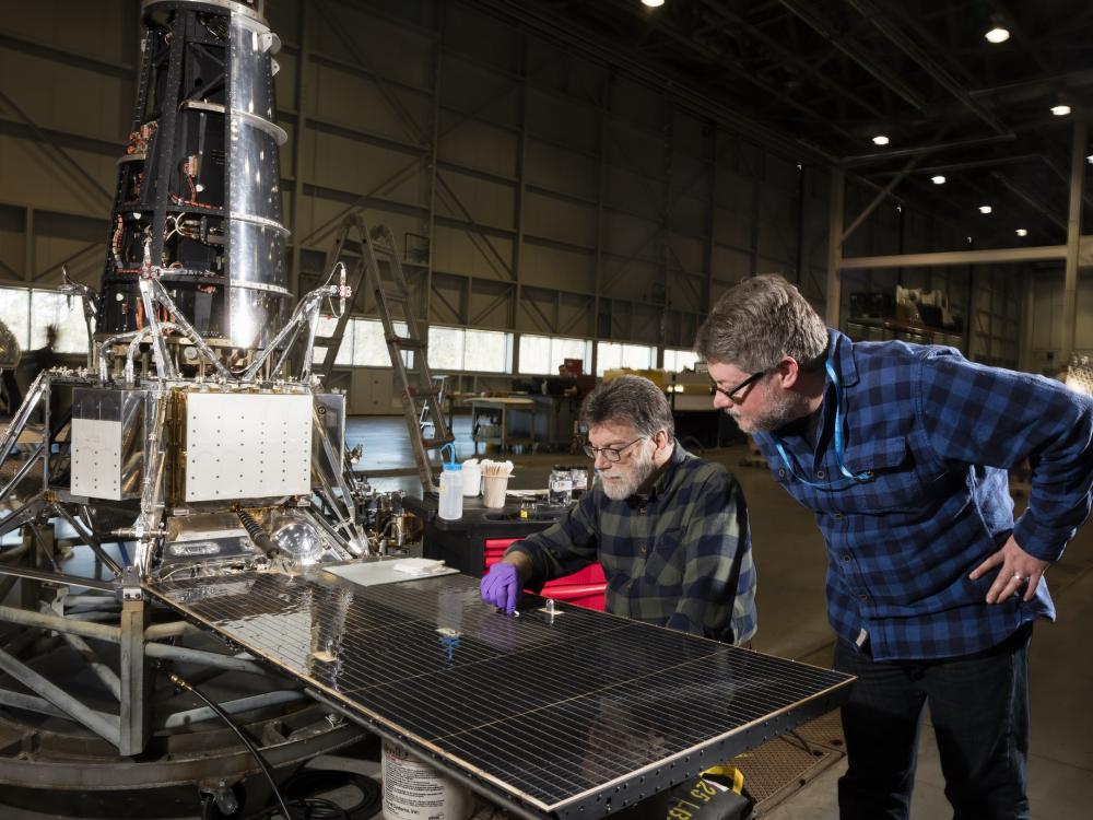 Two men look at a shiny plate on a piece of spacecraft. 1