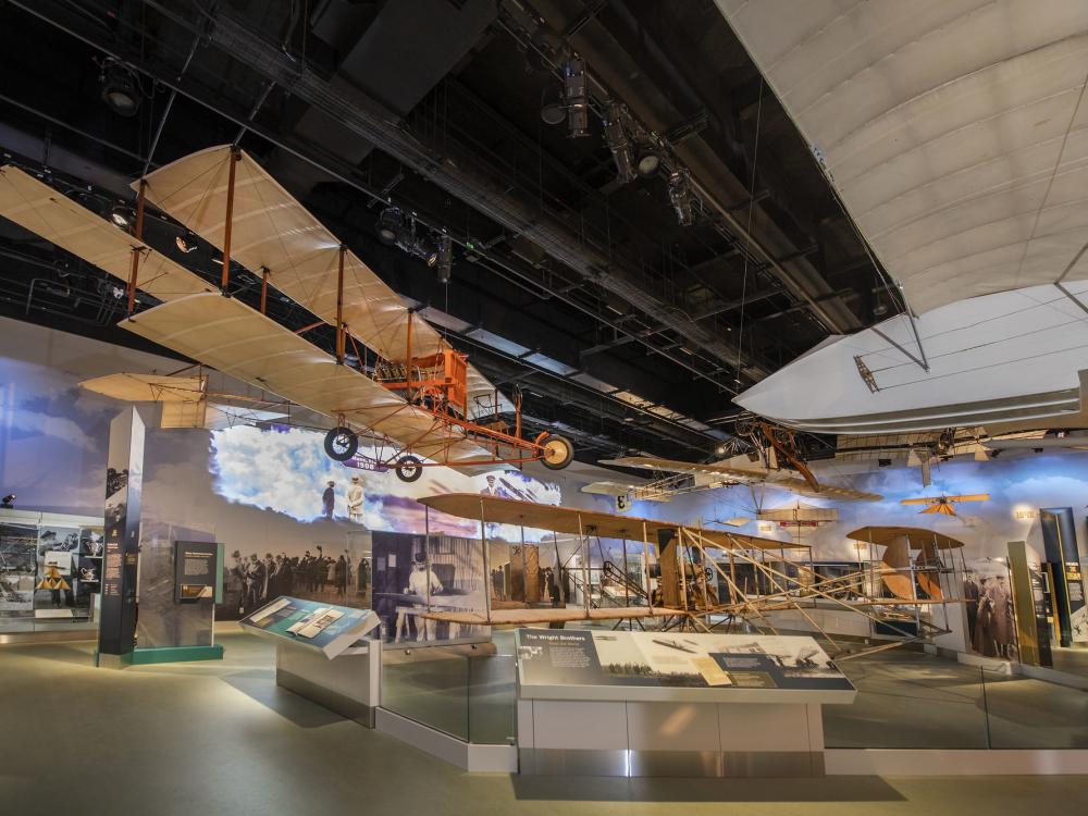 A view of the Early Flight gallery. Several biplanes are on view suspended from the ceiling. 