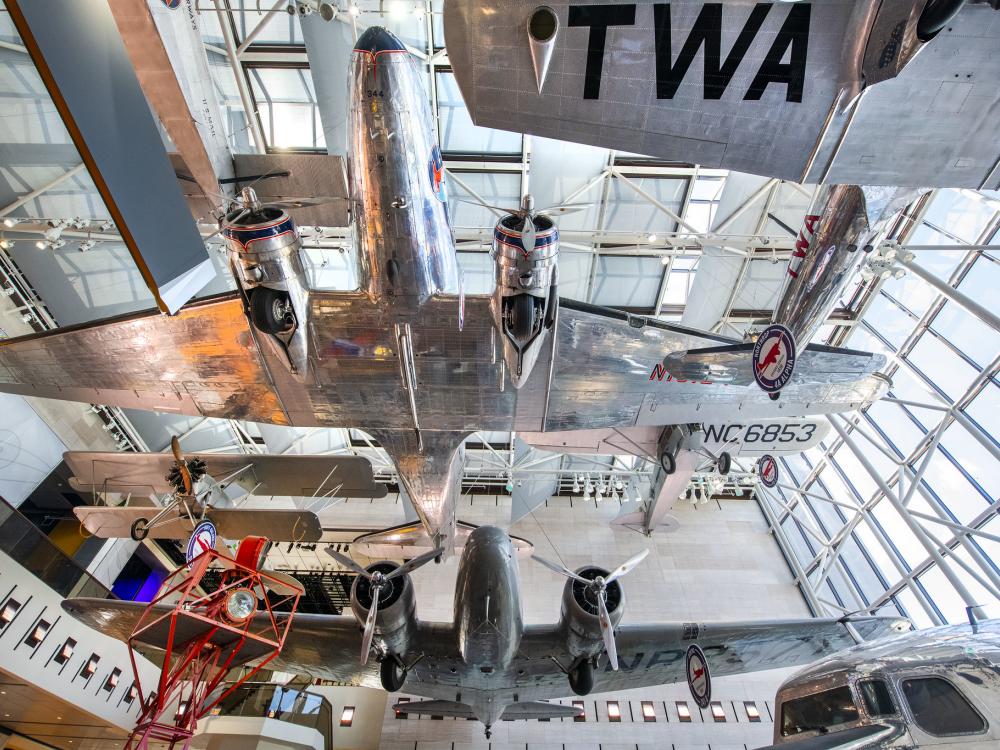 A view looking up from below at the silver bottoms of many suspended airplanes. 
