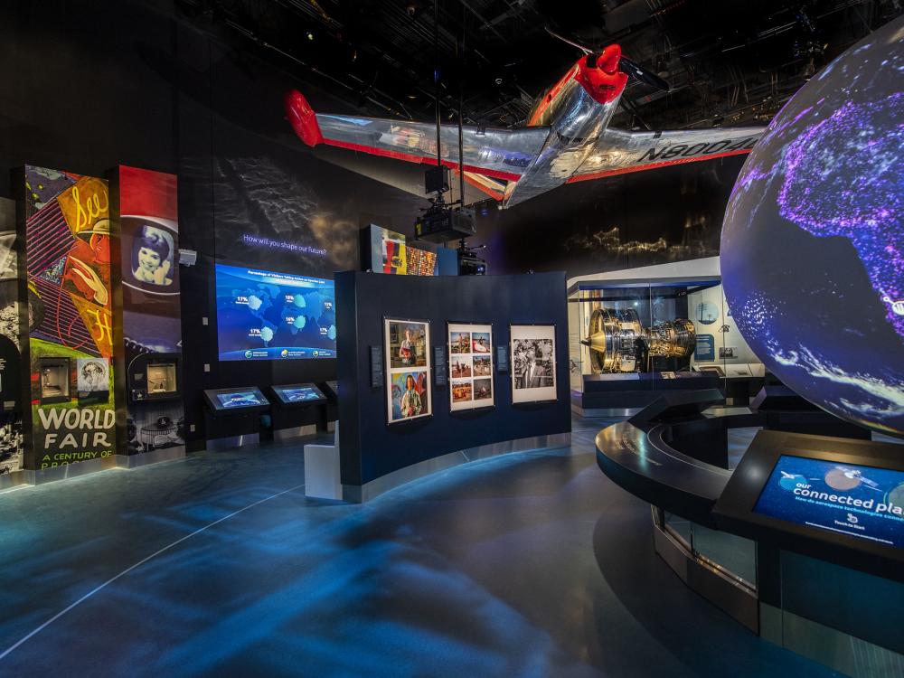 A view of the One World Connected gallery featuring a large globe, a plane, and signs on the walls. 
