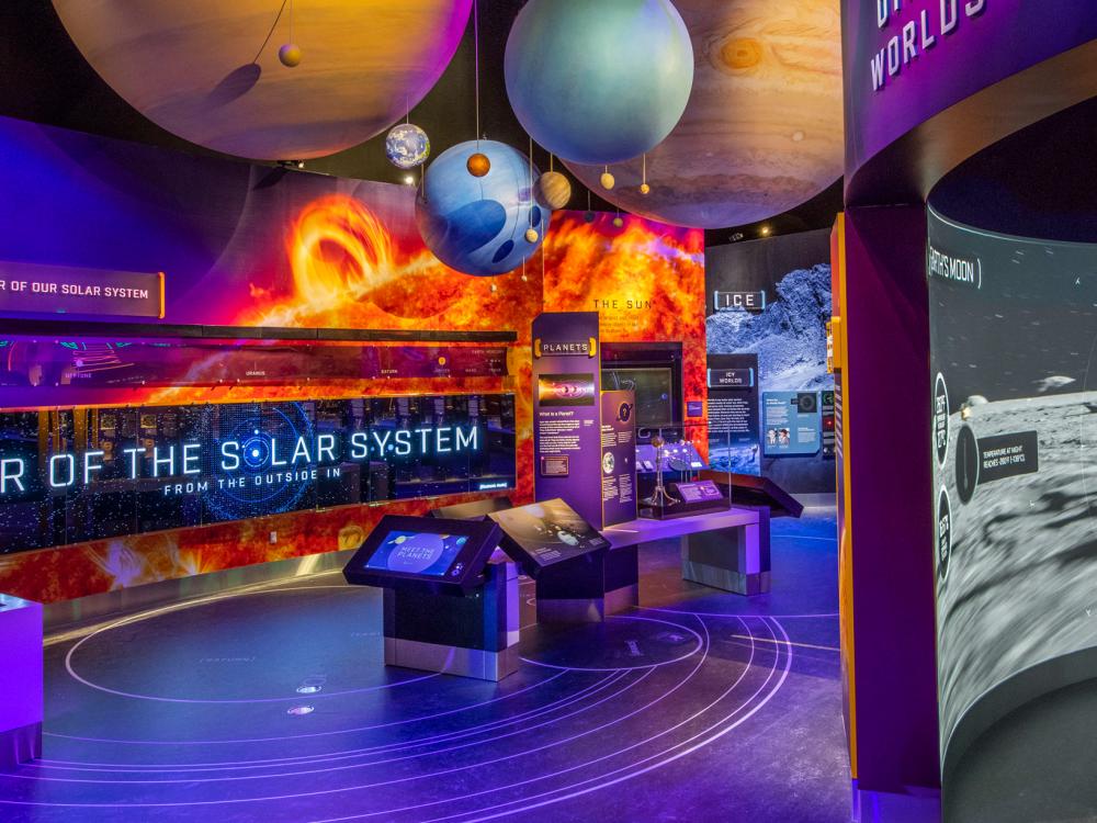 A photo of of exploring the planets gallery. A large sign reads Tour the Solar System and planets hang from above.