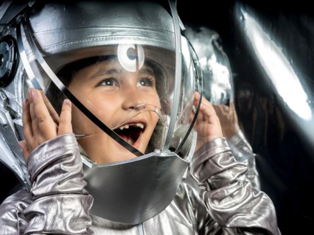 A kid tries on a shiny spacesuit.