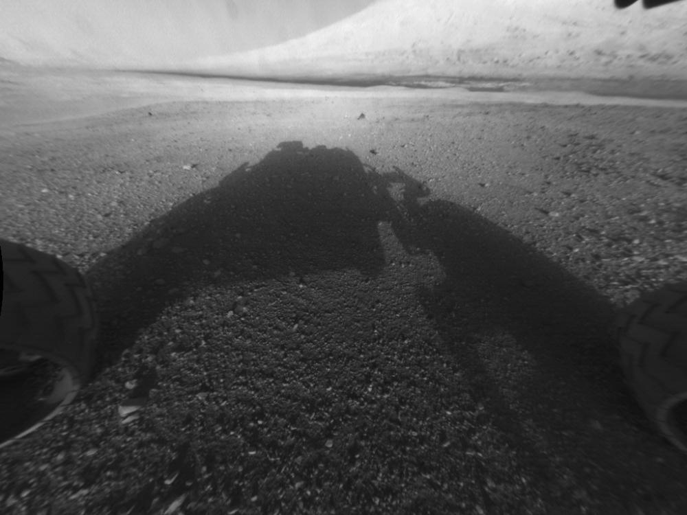 A shadow of a rover is seen in this image. A mountain is in the distance.