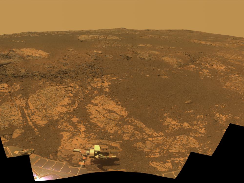 A panoramic view looking out over a hill of the dusty red terrain on Mars.