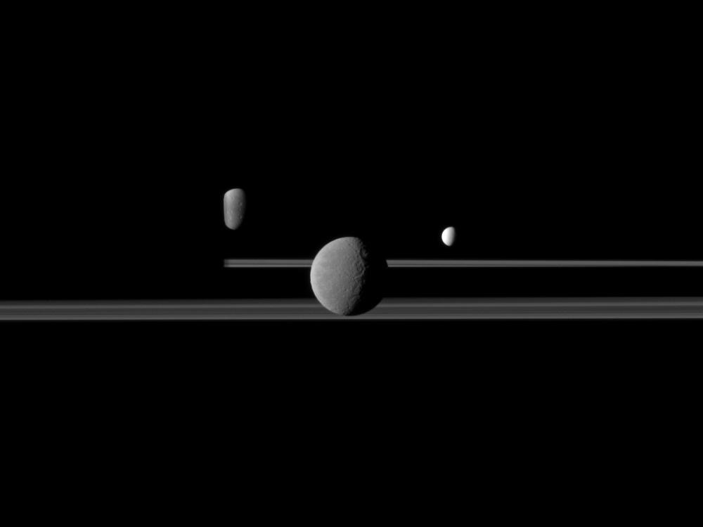 Three moons against a dark background. The moon in the middle appears to be the largest while the moons to the left and right are much smaller looking.