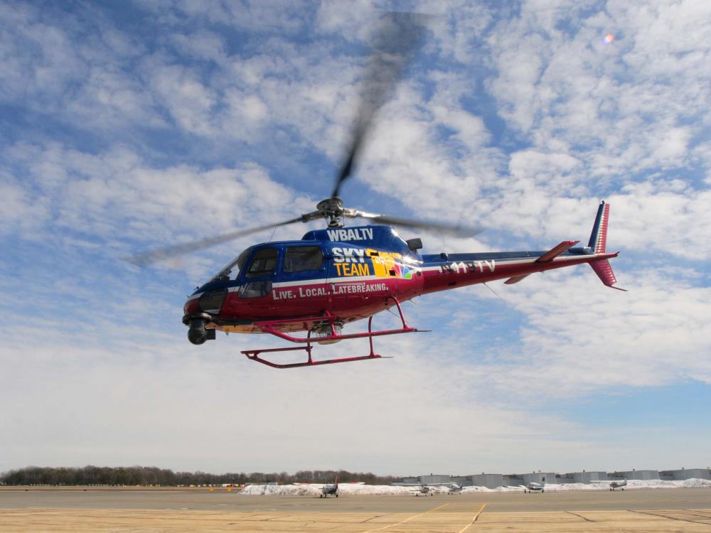 A red and blue helicopter flies above the ground. 