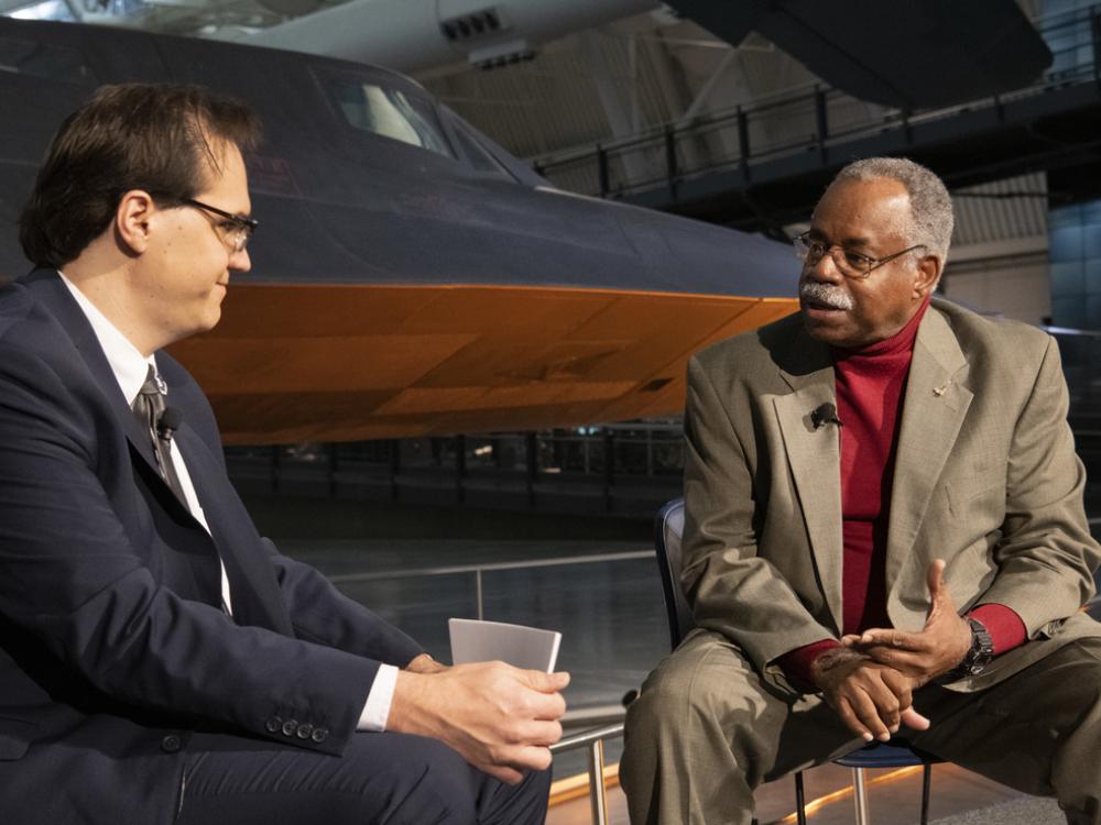 Two men sit and talk together in front of the Blackbird SR-71