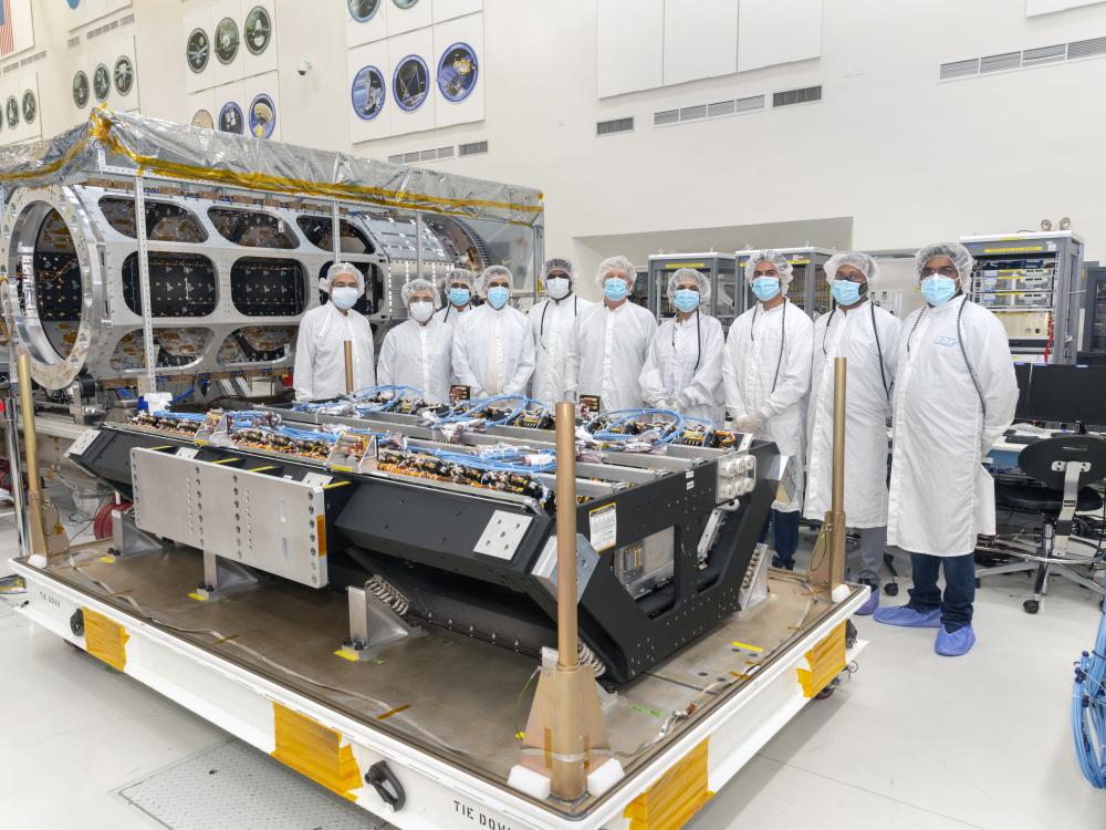 A group of people in clean-room outfits standing behind a spacecraft instrument