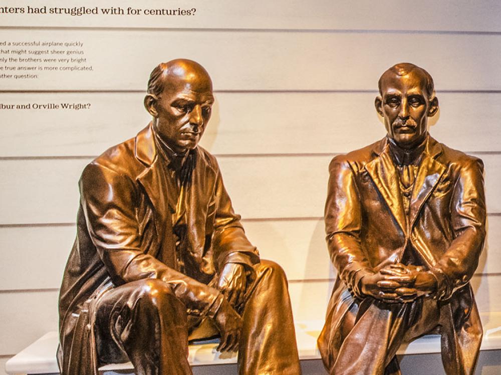 Bronze statues of two seated men in suits. One has a mustache.