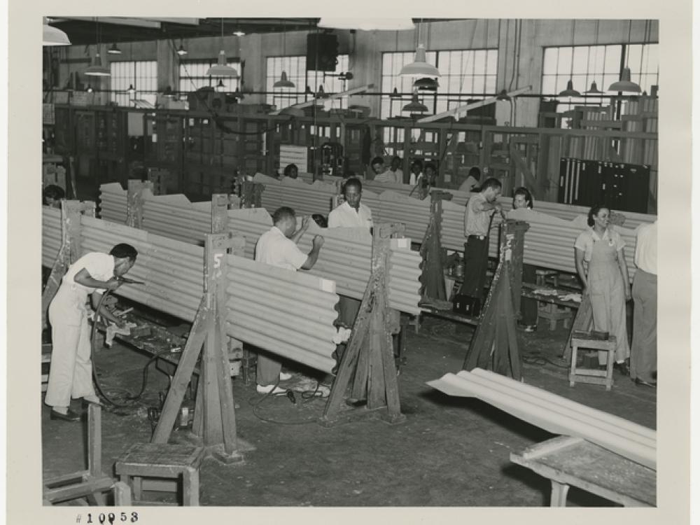 Black and white photo of men and women working on corrugated metal