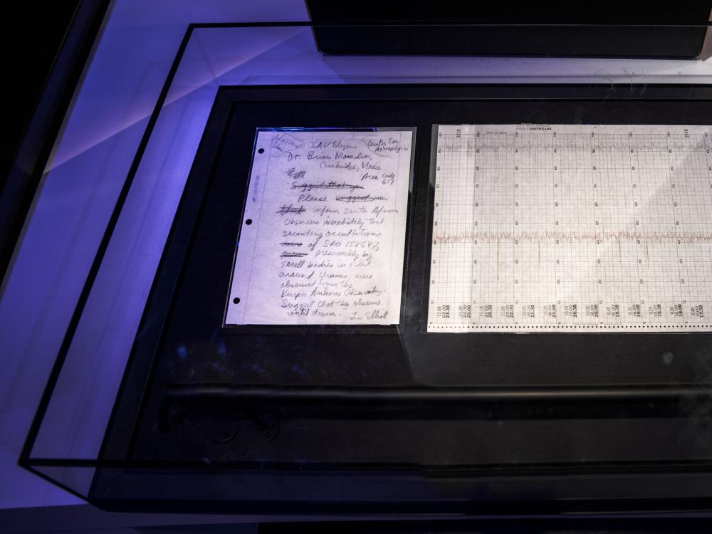 A handwritten letter describing the discovery of rings around Uranus next to a chart demonstrating the discovery. Both are in a display case.