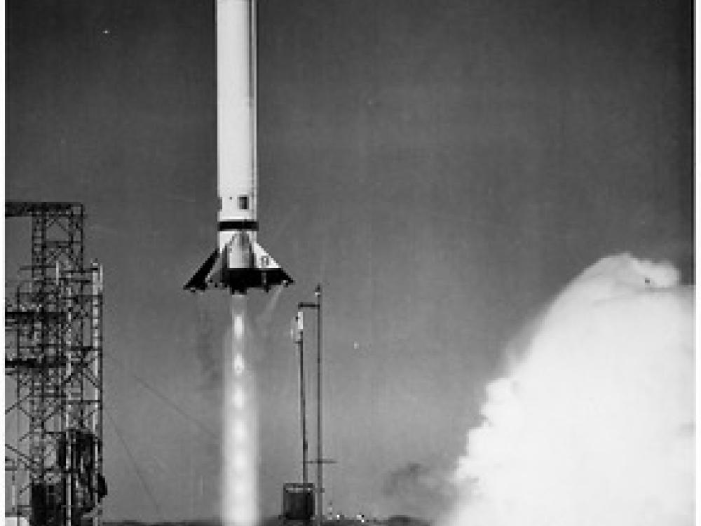 A rocket taking off from its launch pad. The rocket is a light color and looks to have just left the ground. Smoke bellows up from below the rocket.