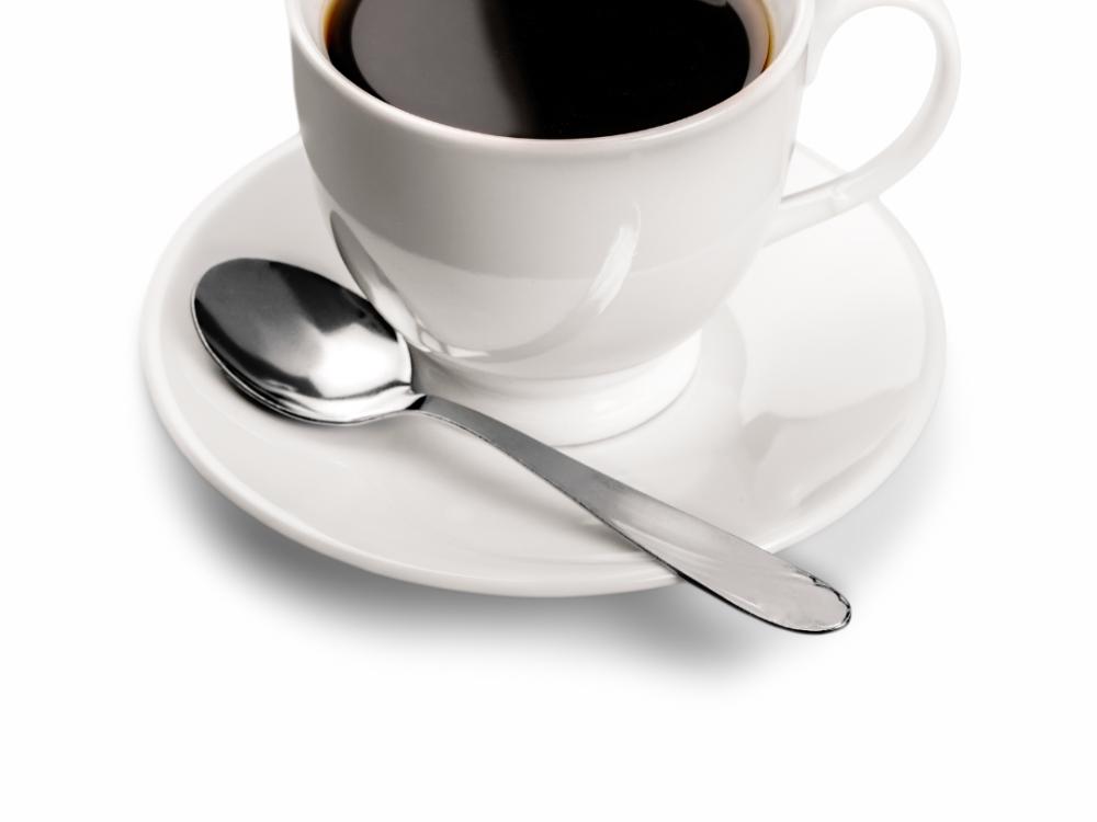 A white cup and saucer and a silver spoon. Black coffee is in the cup. 