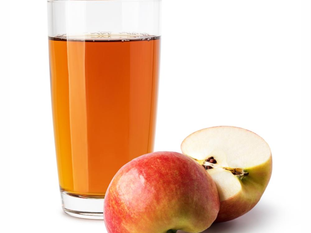 Apple juice in a glass. A halved apple sits next to the glass. 