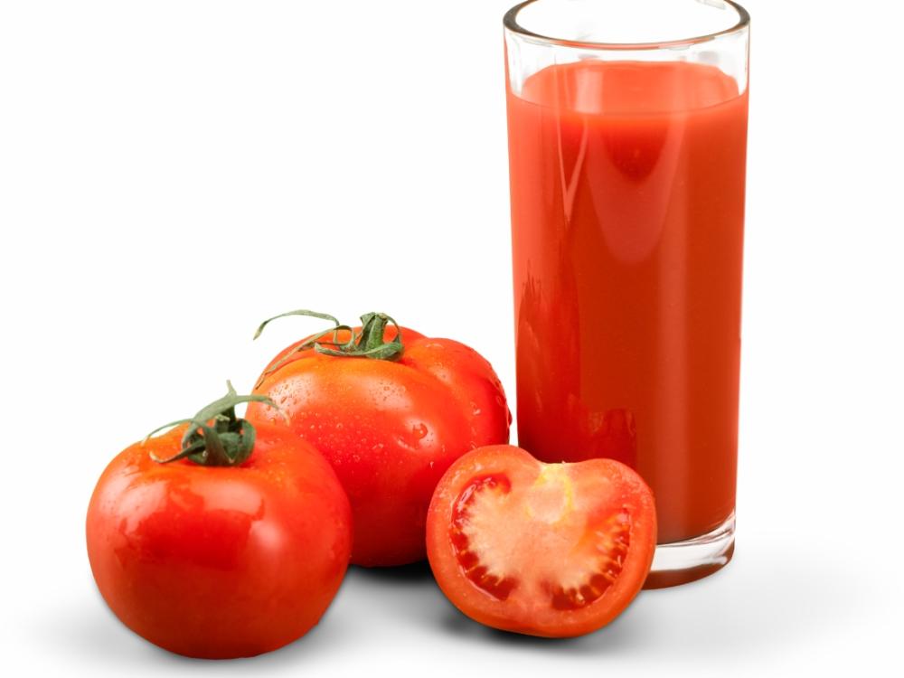 A glass with tomato juice in it. Tomatoes sit next to the glass.