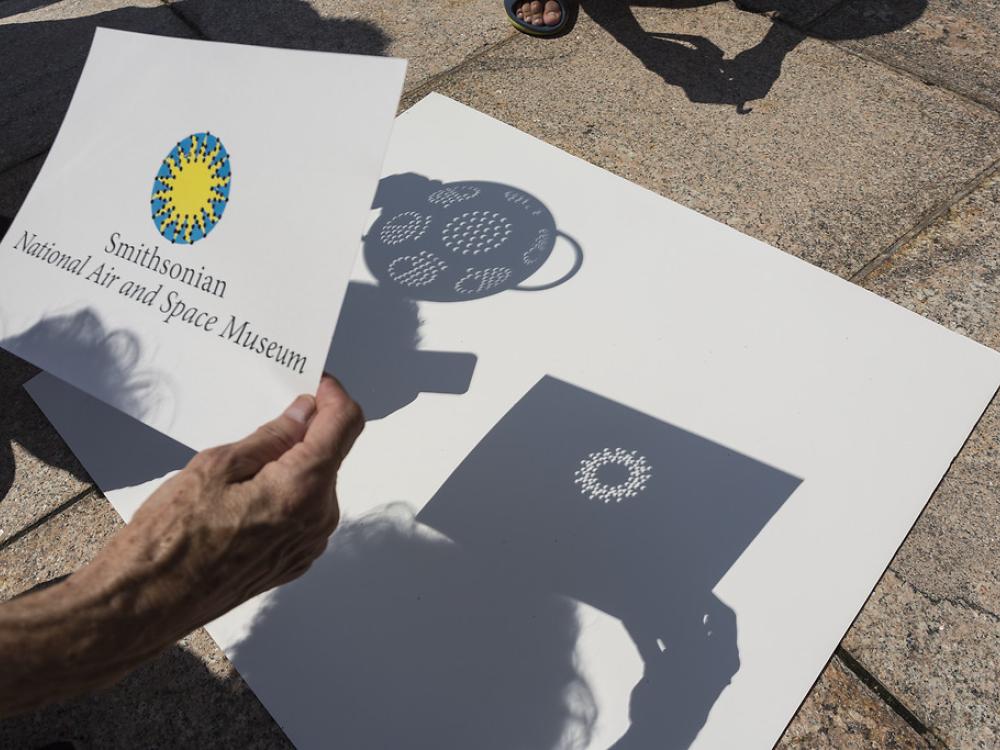 A sheet with hole-punches in the Smithsonian logo creates art with crescent projections on a sheet of paper.