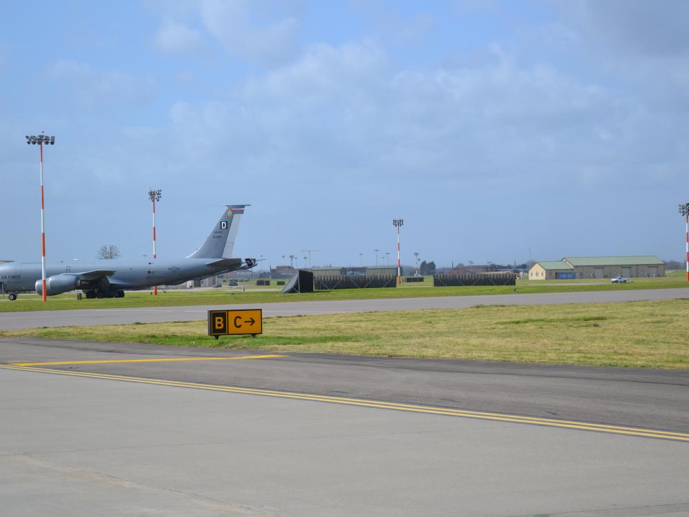 A large aircraft on a runway where a taxiway sign is visible.