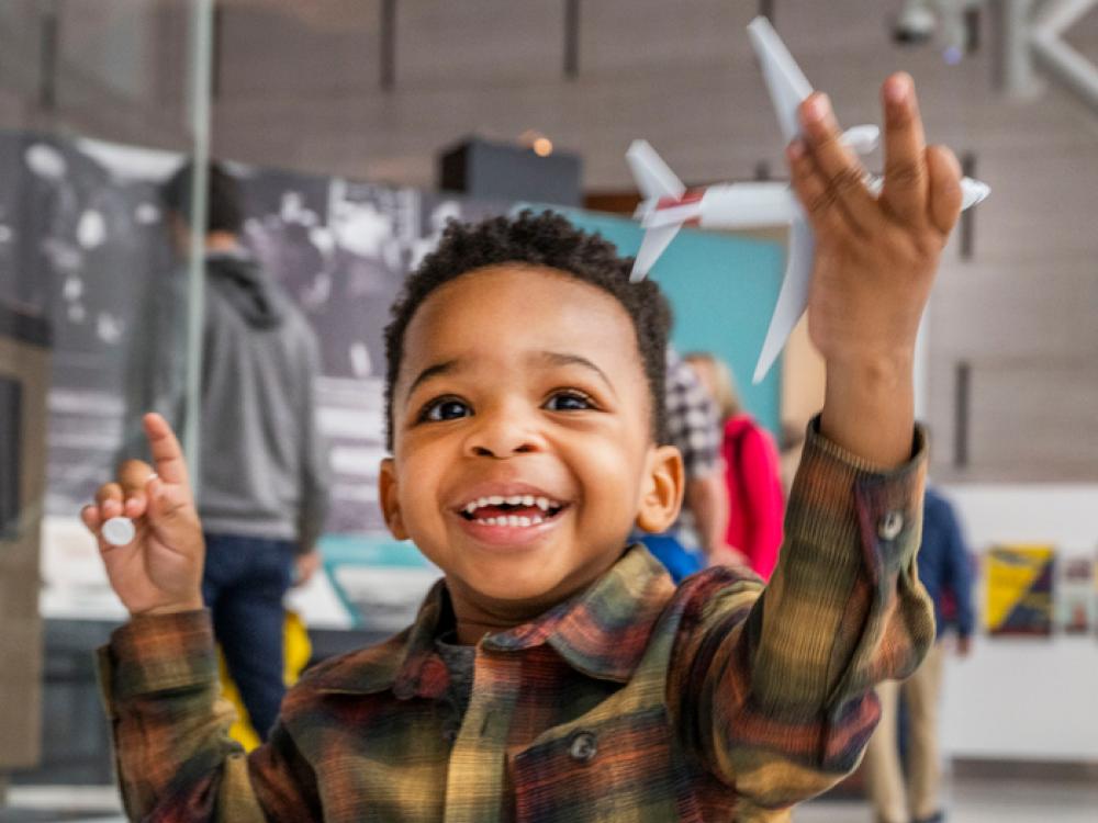 A young child with joy on his face holds up an airplane at Soar Together. 