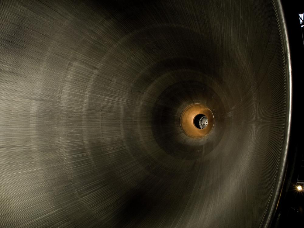 A photo looking into the base of a large metal, hollow, cone, which takes up the majority of the frame. At the point of the cone the metal changes to a rust and orange type color. 