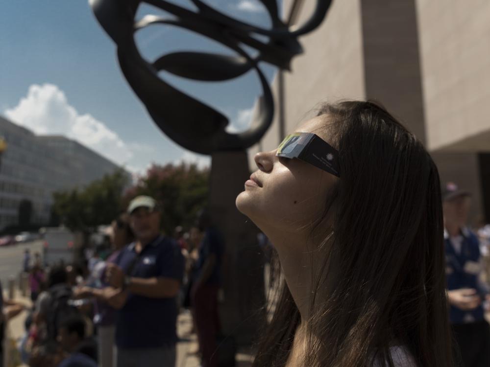 A woman safely stares at the Sun using eclipse glasses at the National Air and Space Museum. 