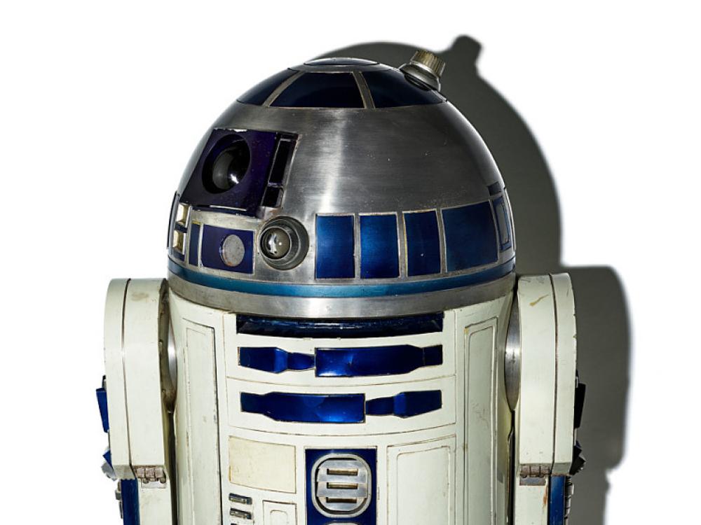 A small droid that looks a little like a roving trash can, its silver and white with blue accents. It's domed top has a lens that gives it an eye-like affect. 