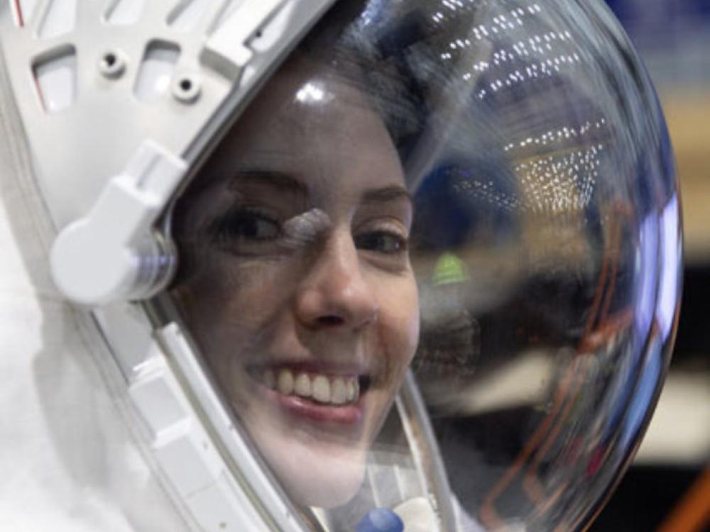 Photo of NASA engineer Christine Jerome wearing a space helmet with a clear visor. She has her head turned to the camera and is smiling. Only her head and the helmet are visible in the photo.