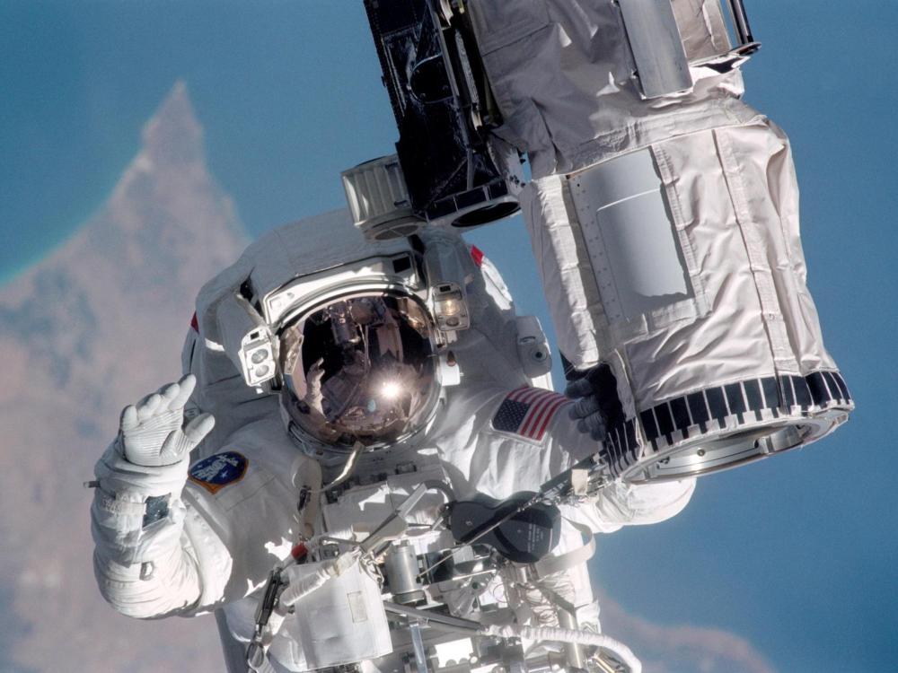 An astronaut in a classic white spacesuit floats with Earth hazy below him or her.