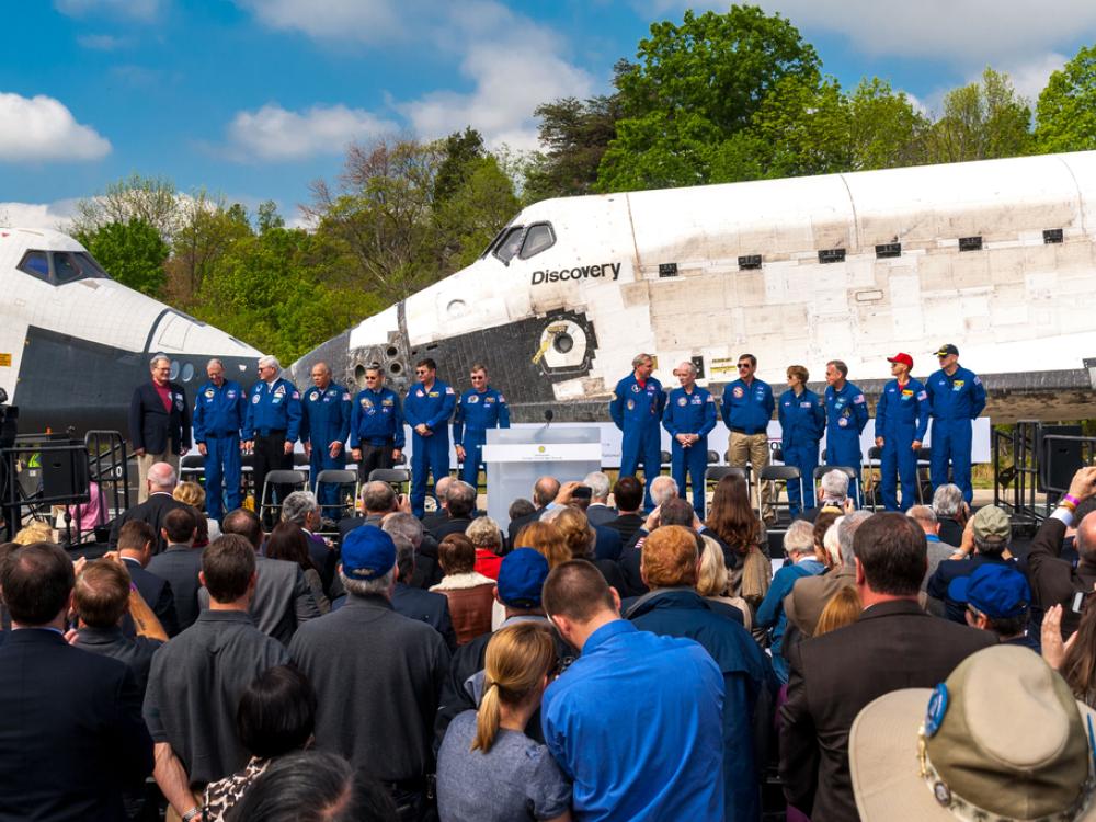 A group of astronauts stand next to two space shuttles that are nose to nose.