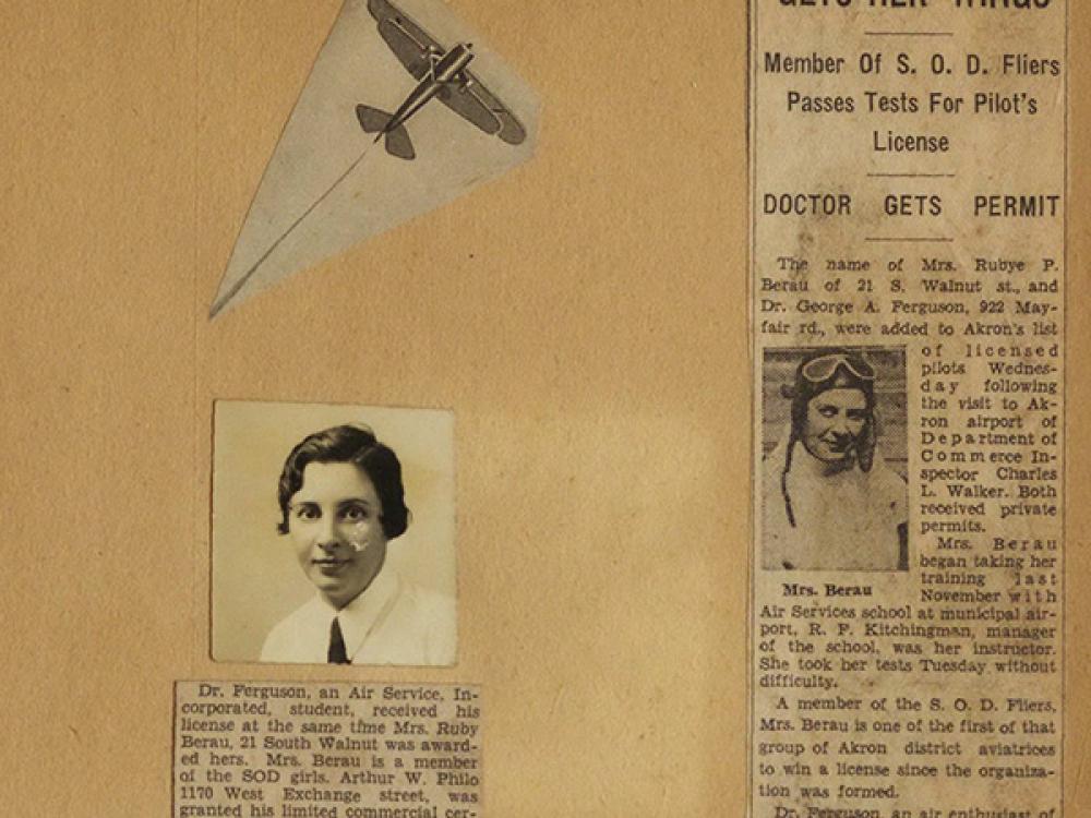 An excerpt of Rubye Berau's scrapbook dated August 23, 1932. There are two newspaper clppings, one titled "Mrs. Rubye Berau Gets Her 'Wings.''" There's also a small image of an airplane and a black and white photograph of Berau, a woman with a short haircut and a tie. 