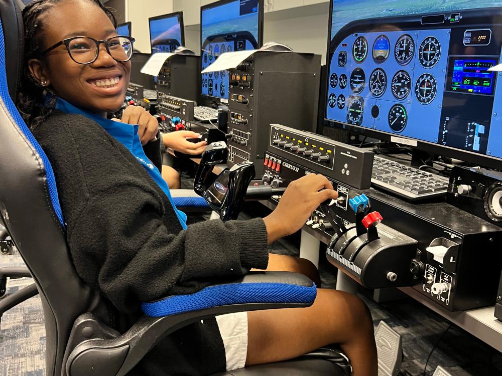 A teenaged Black girl sits at a complicated simulator. 