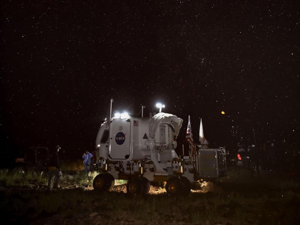 A small white mobile unite with NASA' logo stands under a starry sky.