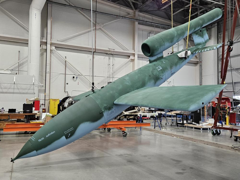 A missile with fresh new paint hangs diagonally from the ceiling in a hangar.