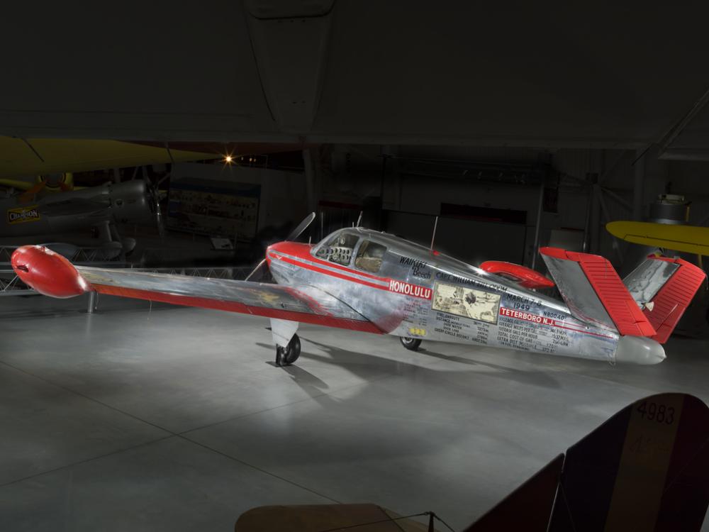 Silver and red painted single engine aircraft with V-tail. 