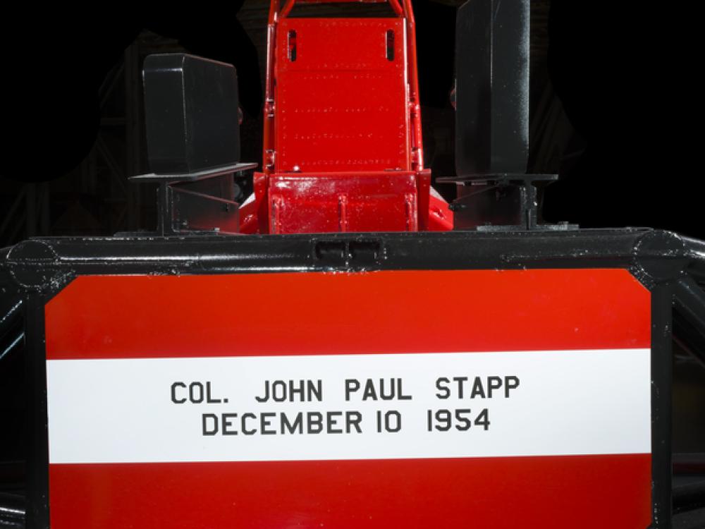 Straight metal seat attached to the middle of a rocket sled. Col. John Paul Stapp December 10 1954 is painted on the seat. 